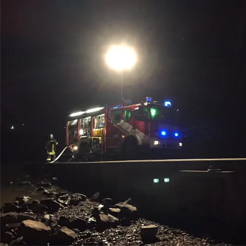 Hilfeleistungslöschfahrzeug der Feuerwehr mit ausgefahrenem Lichtmast bei Nacht