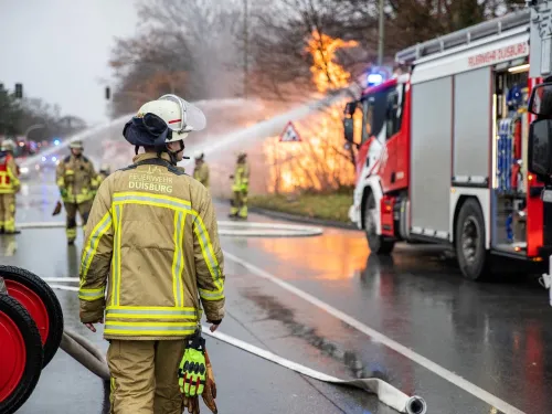 Hilfeleistungslöschfahrzeug der Feuerwehr neben einem brennenden Gebäude