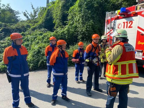 Jugendfeuerwehr-Gruppe im Gespräch mit Gruppenführer vor einem Löschfahrzeug